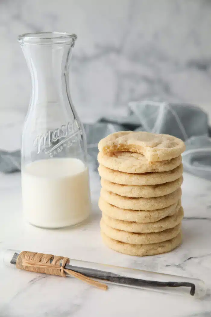 Stack of basic sugar cookies next to a pitcher of milk.