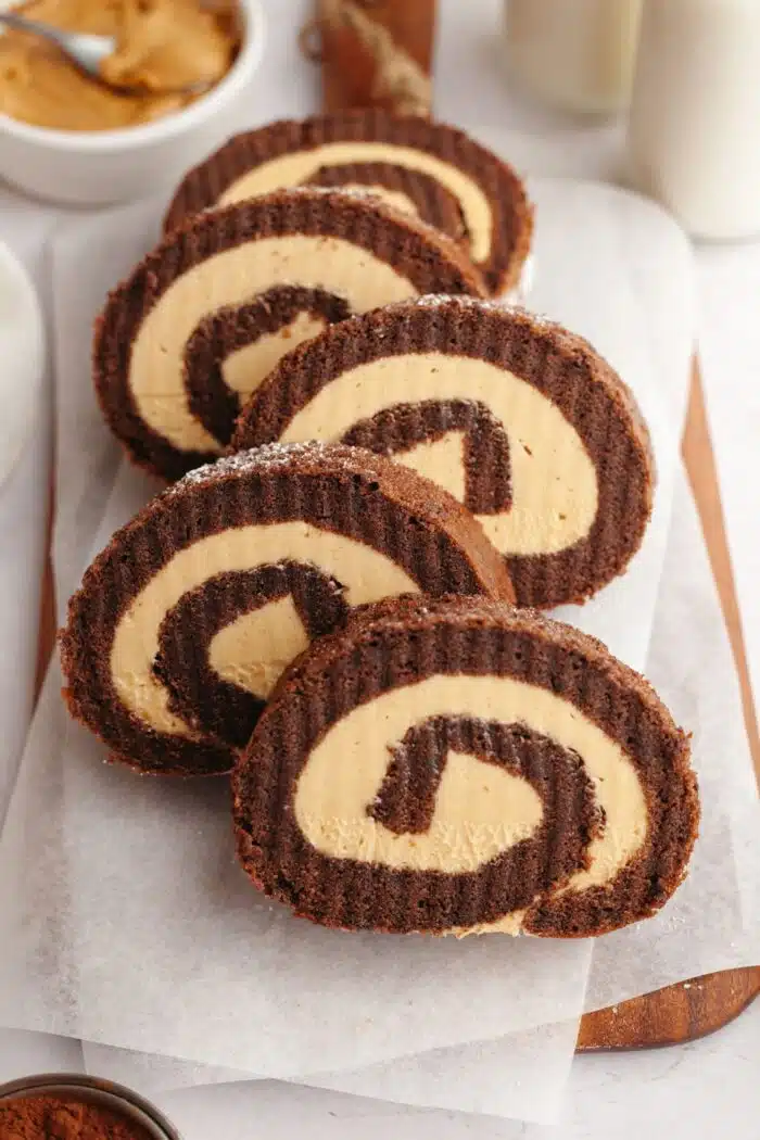 Slices of chocolate peanut butter cake roll staggered on a wooden cutting board.