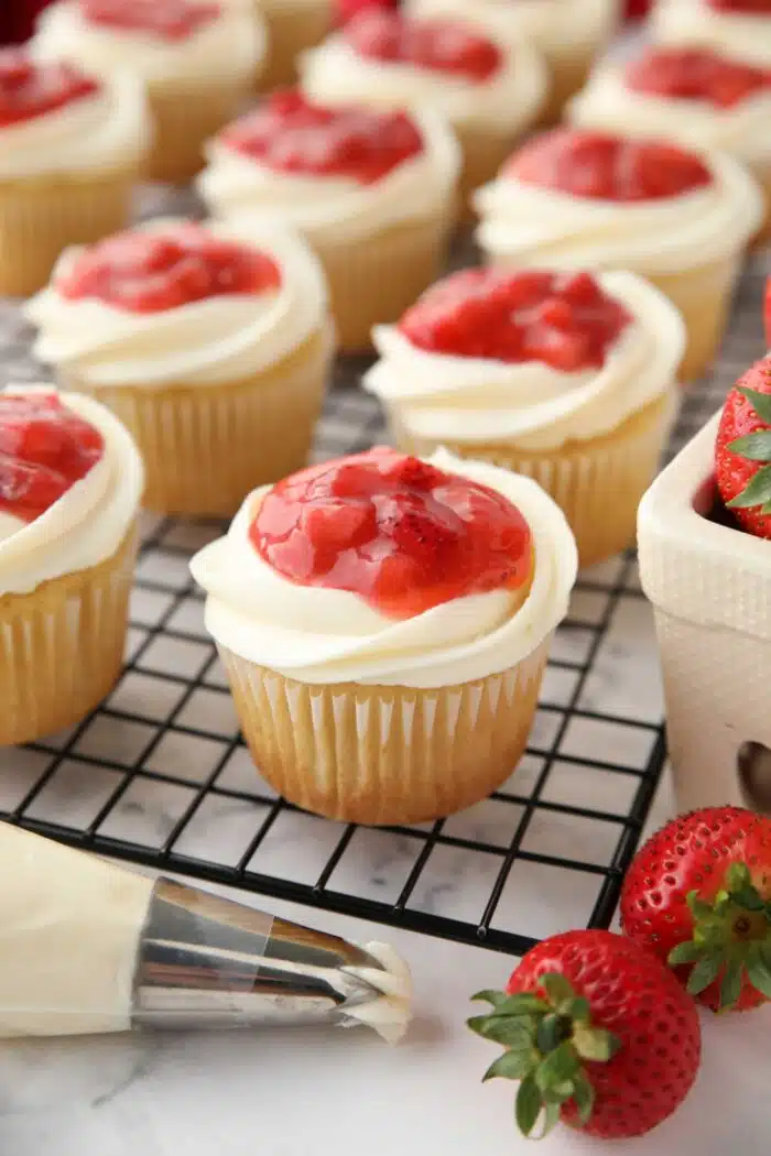 Strawberry Shortcake Cupcakes with strawberry sauce on top of whipped cream cheese frosting and a vanilla cupcake.