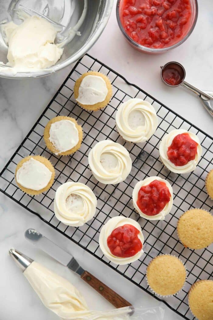 Topping vanilla cupcakes with whipped cream frosting and strawberry sauce to make strawberry shortcake cupcakes.