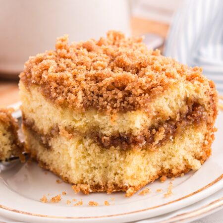 Cinnamon crumb cake on a plate with a forkful taken out and a cup of coffee in the background.