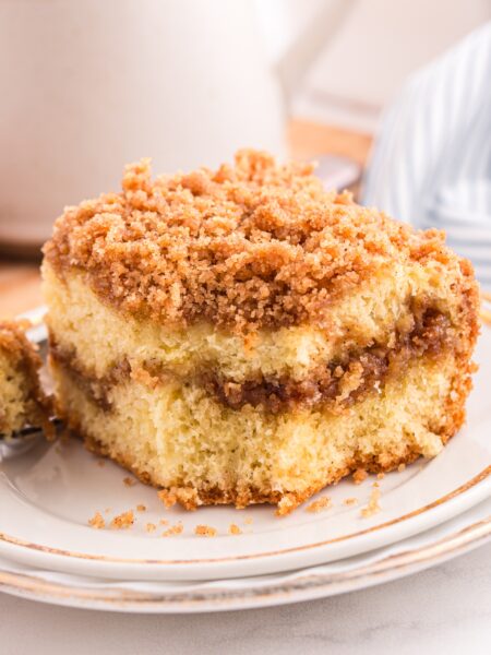 Cinnamon crumb cake on a plate with a forkful taken out and a cup of coffee in the background.