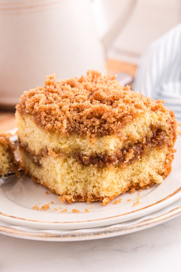 Cinnamon crumb cake on a plate with a forkful taken out and a cup of coffee in the background.