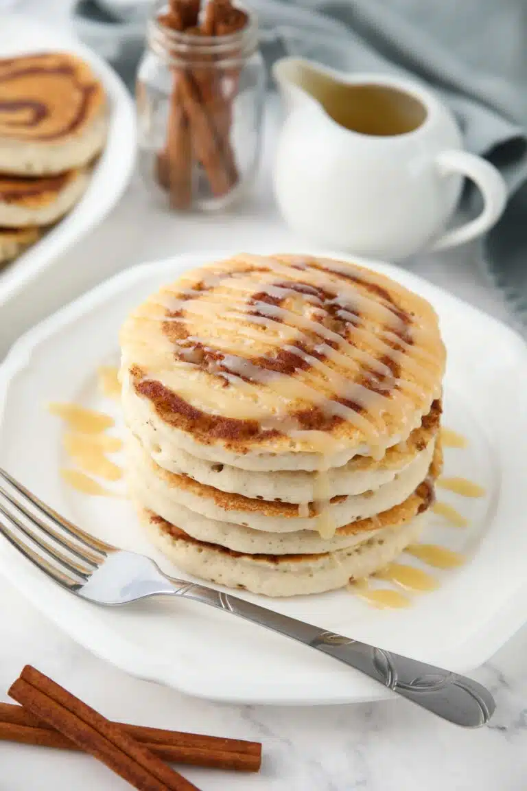 Stack of cinnamon roll pancakes with cream cheese glaze drizzled on top.